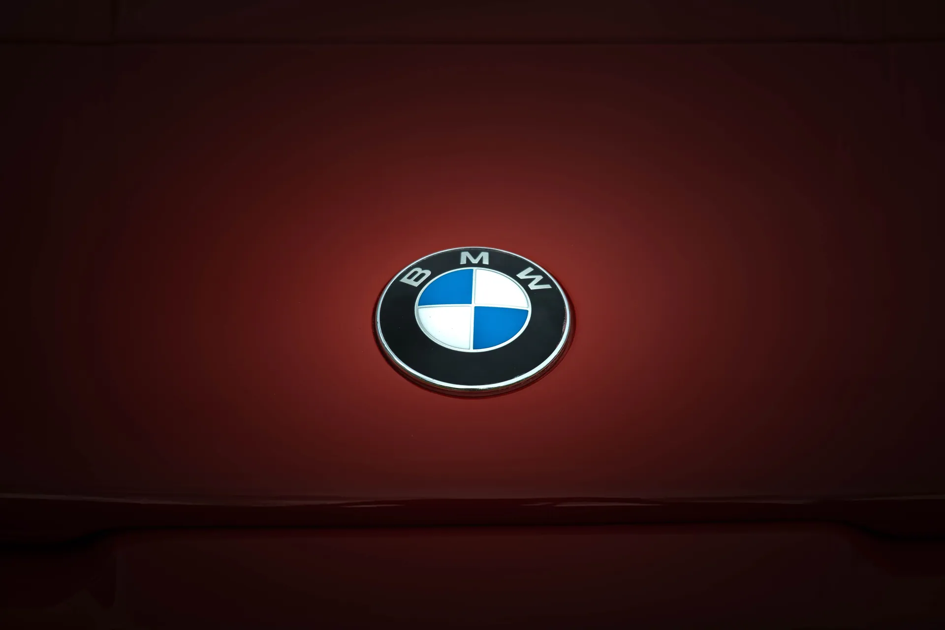 Close-up of BMW emblem on a glossy red vehicle surface, emphasizing modern design.
