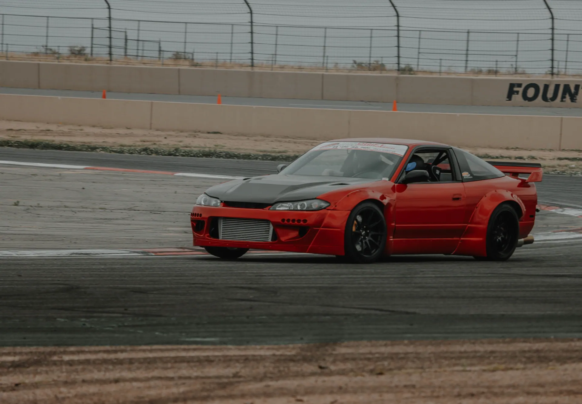 Red Nissan racecar drifting on a racetrack during a day event. Captured with dynamic motion.