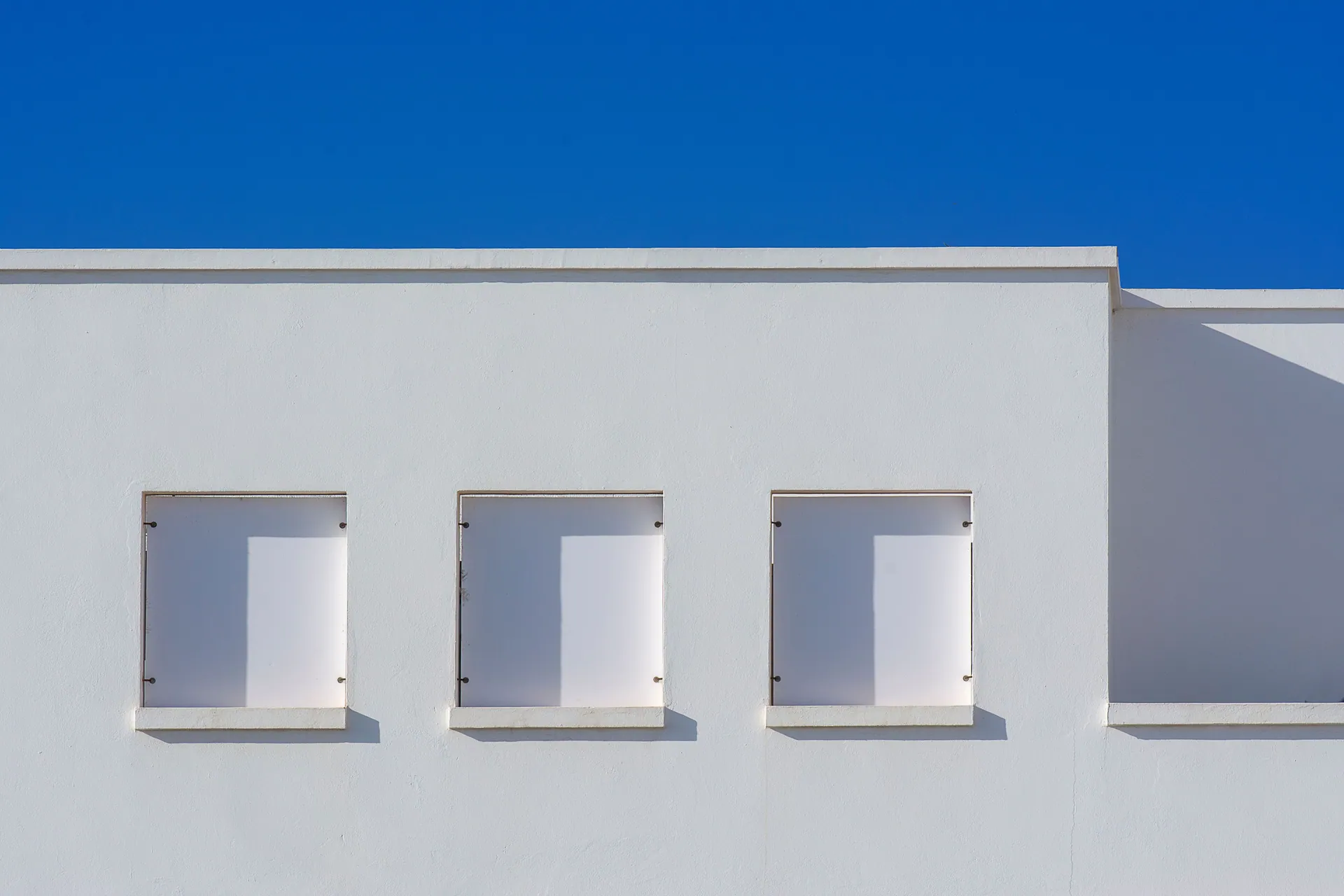 A minimalist white building facade with three windows and a vibrant blue sky backdrop.