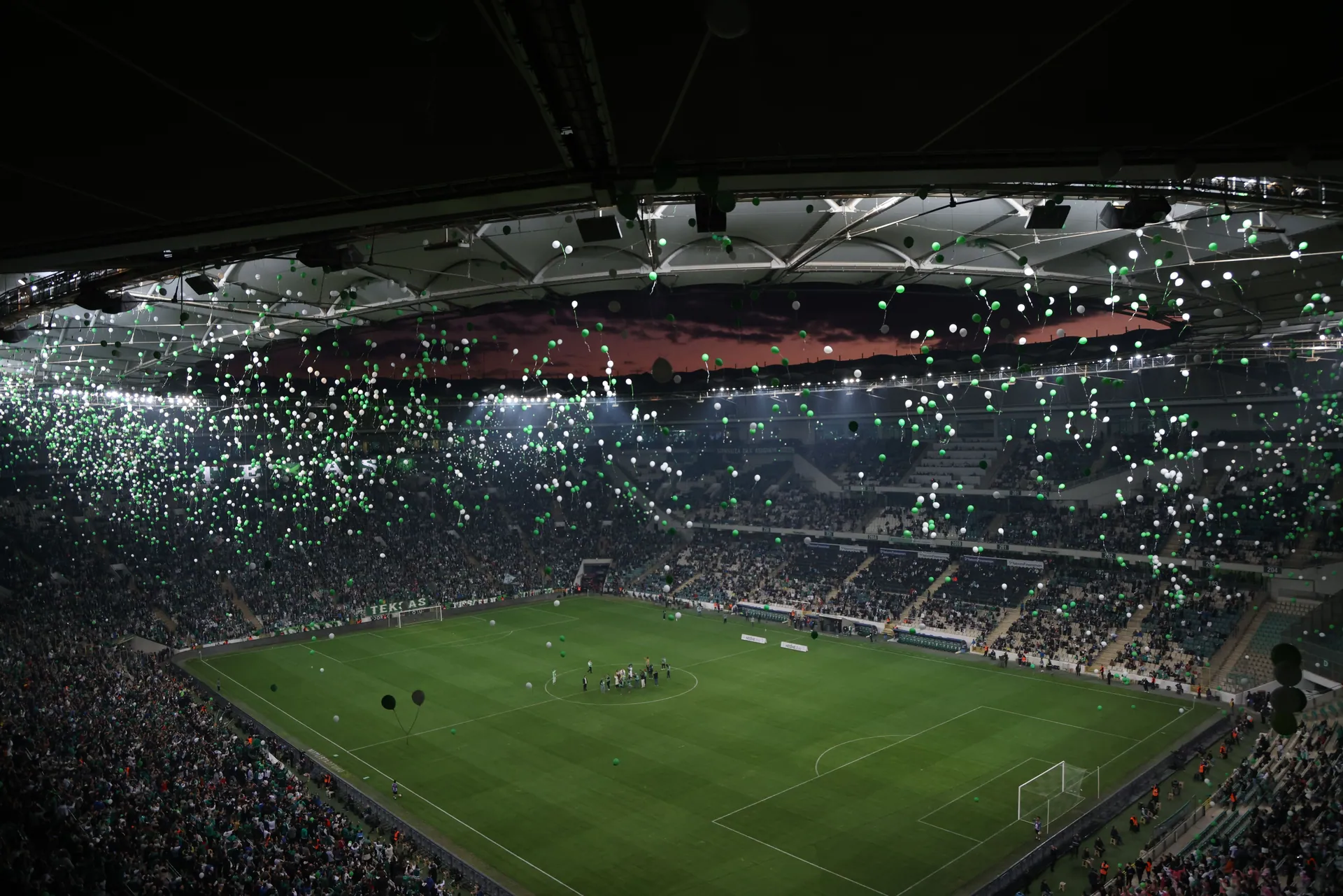 A crowded stadium at twilight with balloons filling the sky, creating a festive atmosphere.