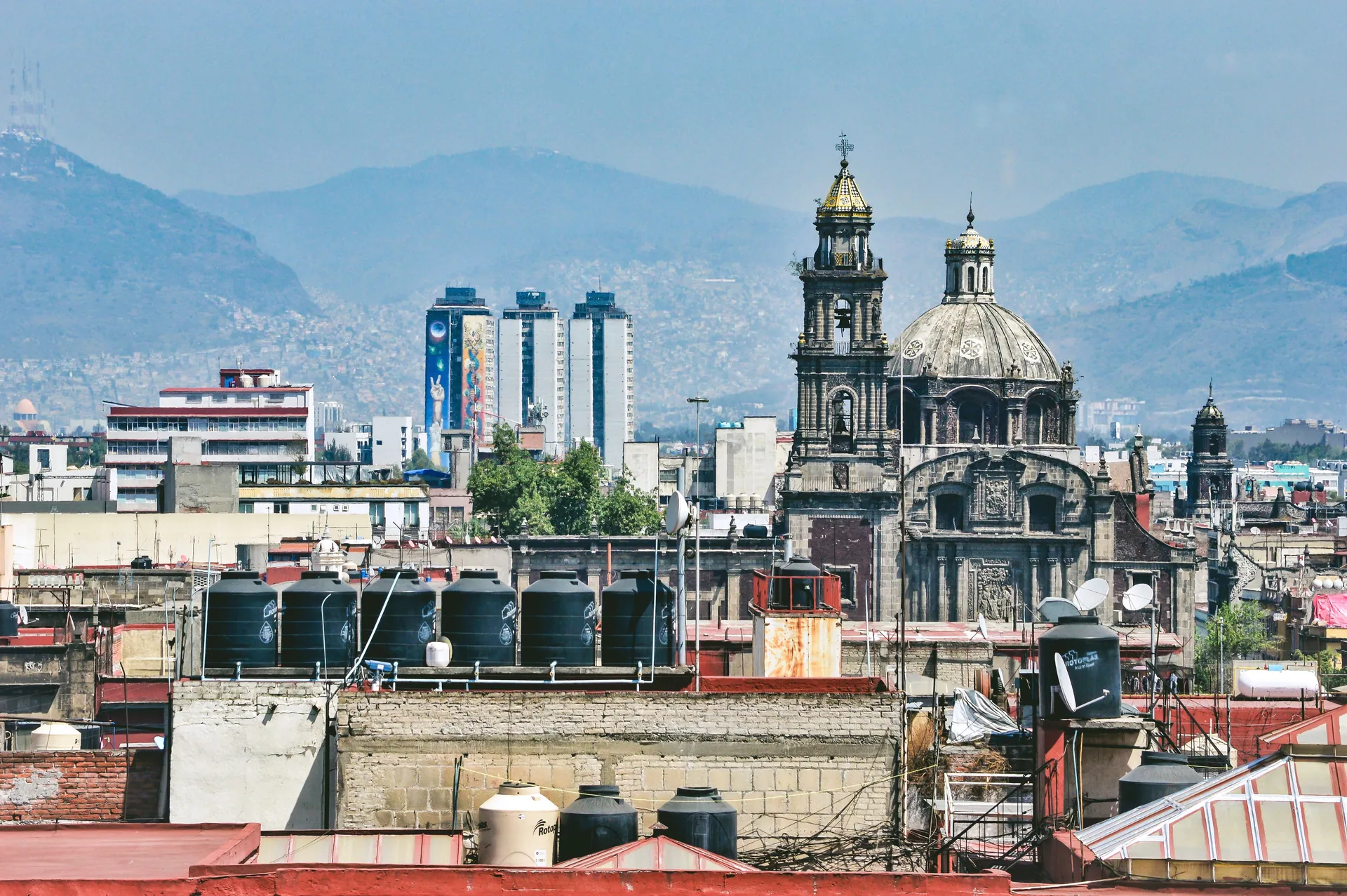 A stunning view of a historic church amidst Mexico City's urban architecture, with mountains in the background.
