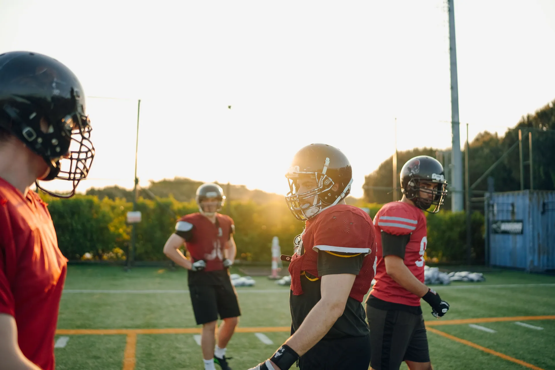 Football players practicing on a field at sunset, wearing gear and helmets.