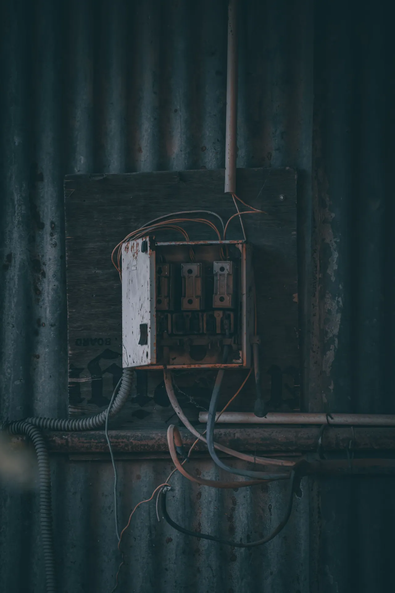 A rusty electrical panel with visible wires on a corrugated metal wall, depicting urban decay.
