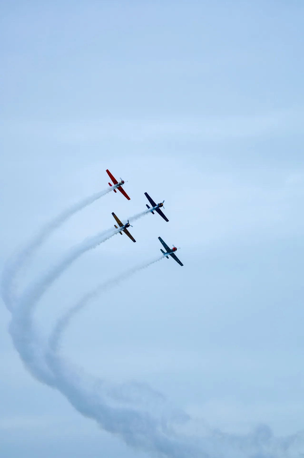 Trio of colorful aerobatic planes executing a synchronized air show maneuver against a clear blue sky.