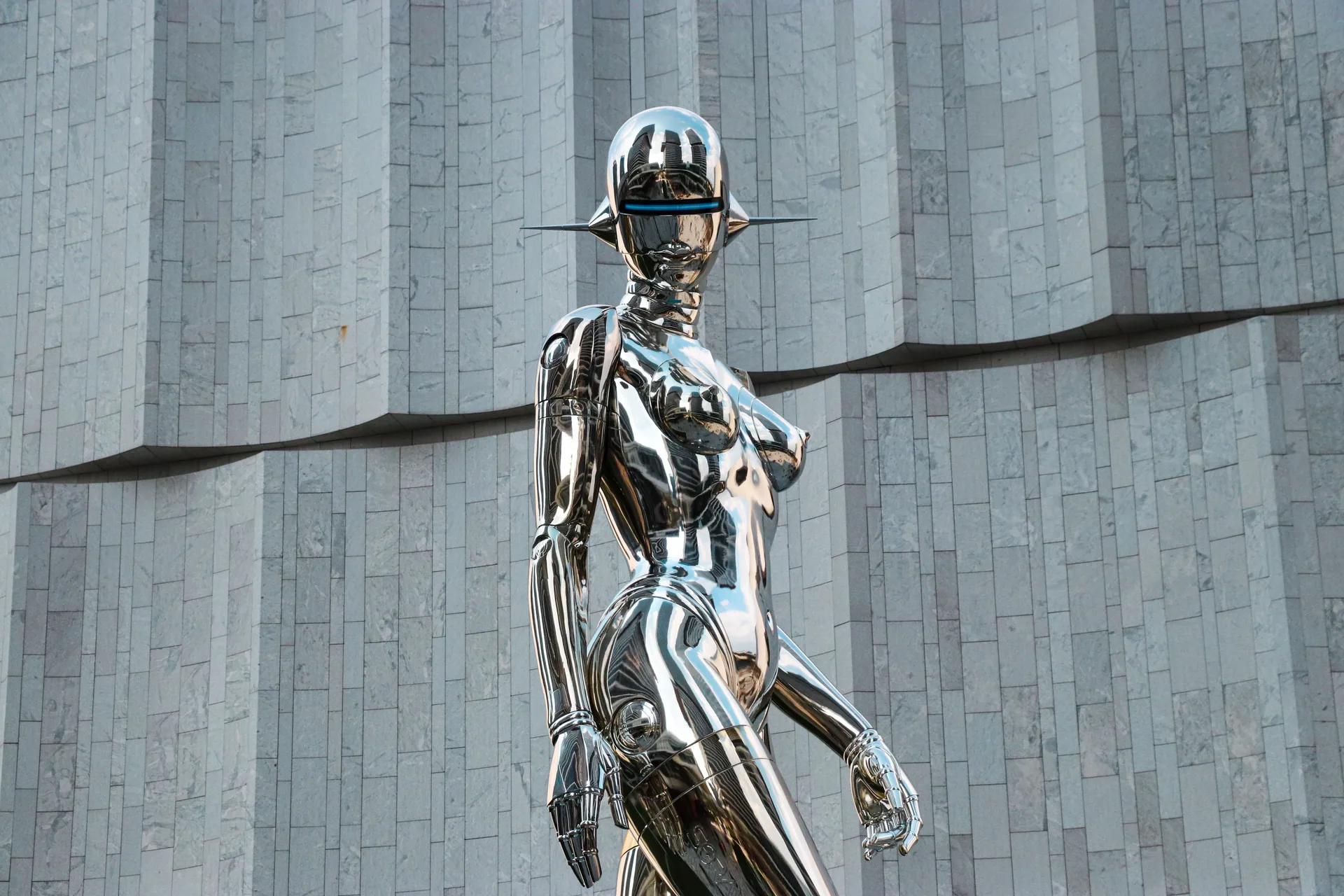 A sleek, chrome humanoid sculpture set before a minimalist, geometric wall.