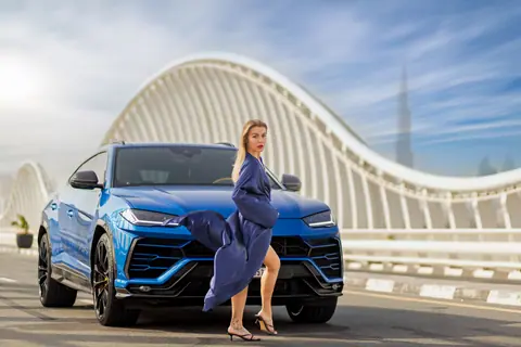 Elegant woman poses in front of a luxury blue SUV on Dubai's iconic Meydan Bridge