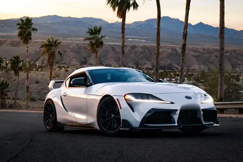 A white sports car parked on a desert highway with mountain views at sunset.