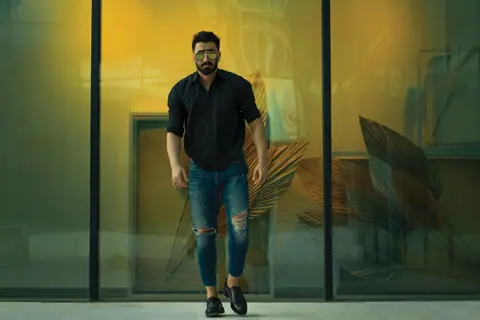 A fashionable man in casual attire walking in front of a modern glass building.