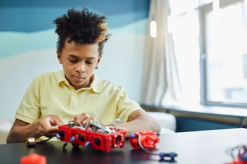 A focused young boy engaged in building a red robotic project indoors.