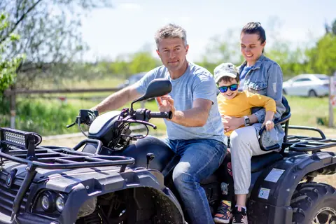 Father, mother, and child enjoying a fun ATV ride outdoors on a sunny day.