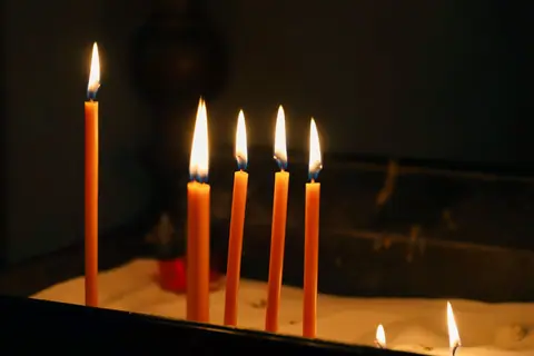 Warm glow of lit candles on a church prayer offering table at night.