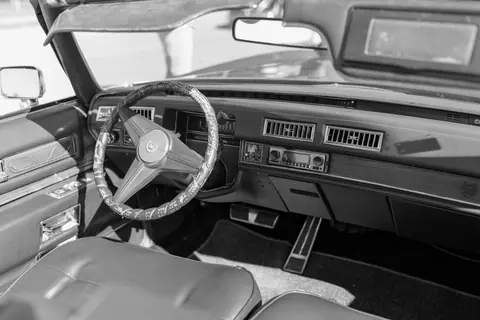 Black and white photo of a vintage car interior with a retro dashboard and steering wheel.
