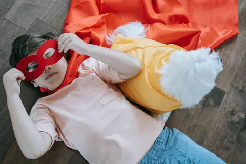 Boy in superhero costume with dog companion, lying on wood floor in playful pose.