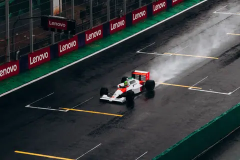 A classic Formula 1 car races on a wet track at Interlagos, Brazil, leaving a trail of spray behind.