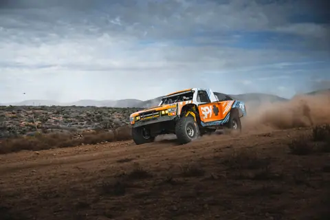 High-speed off-road rally truck kicking up dust in Baja California's rugged desert.