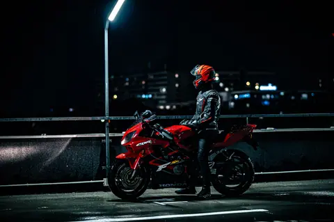 A motorcyclist in full gear on a red motorcycle parked under streetlights in a city at night.