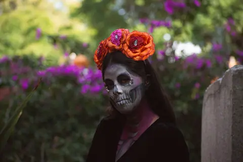 Portrait of a woman with Day of the Dead makeup in a garden setting.
