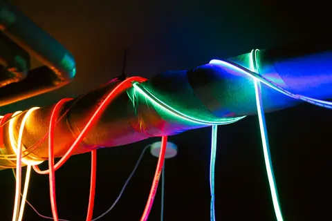 Vibrant LED lights in red, blue, and green illuminating a metal pipe in a dark room.