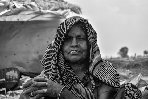 A black and white portrait of a smiling elderly woman wearing a headscarf outdoors.