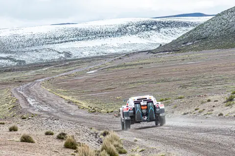Rally car racing along a dirt road in Arequipa, Peru, amidst snowy mountains.