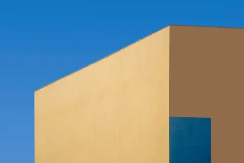 Minimalist architectural shot featuring a modern yellow and blue building under a clear blue sky.