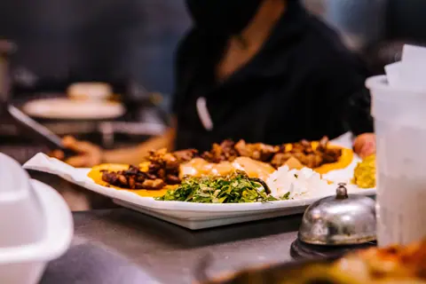 Vibrant Mexican dish with greens, cheese, and meat served on a white plate in a restaurant setting.