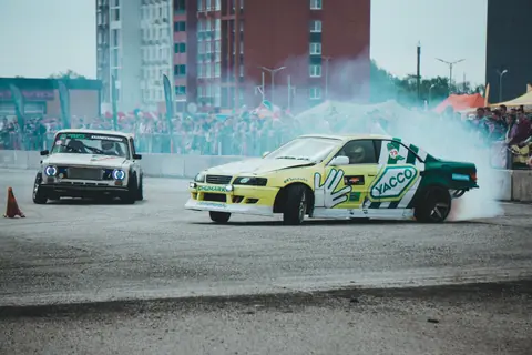 Dramatic scene of a car drifting contest with spectators in an urban environment.