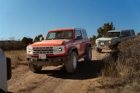Capture the thrill of off-roading with Ford Broncos navigating a rugged desert trail under a clear blue sky.
