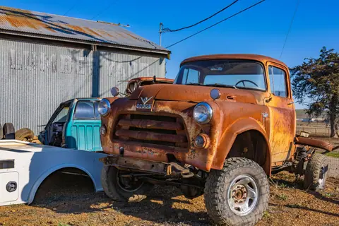 A rusty, vintage Dodge pickup truck parked outdoors in a junkyard setting.