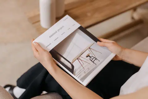 Person relaxing indoors while reading a minimalist design magazine, showcasing modern aesthetics.