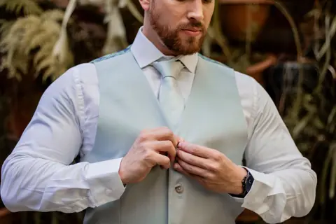 Close-up of a man adjusting his vest, dressed in elegant formal attire.