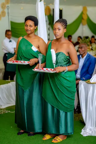 Two African women elegantly dressed in green traditional dresses at a formal event indoors.