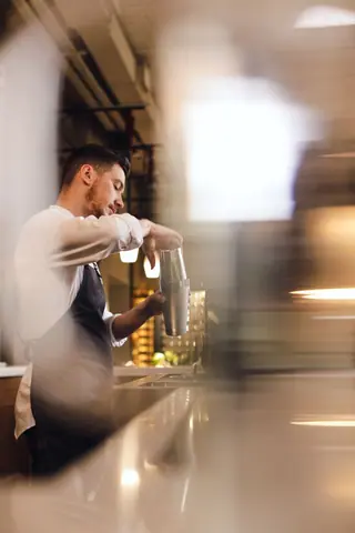 Side view of a bartender skillfully mixing a drink with a shaker indoors.