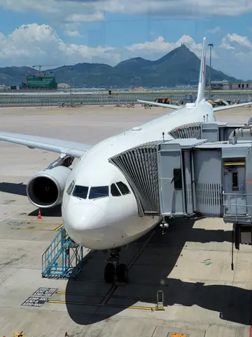 Commercial airplane docked at a boarding gate with mountains in the background.