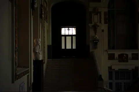 A dimly lit interior hallway featuring classical sculptures and ornate architectural details.