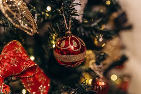 Close-up of a beautifully decorated Christmas tree with a red bauble and warm bokeh lights.