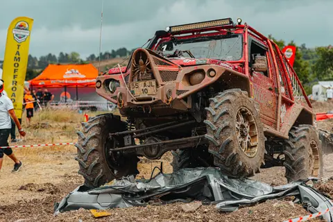 Red off-road vehicle tackling challenging outdoor race through rugged, muddy terrain.