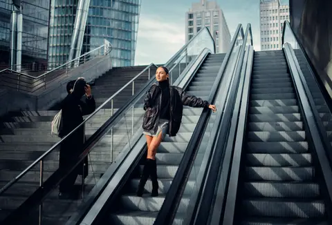 Stylish woman poses on an escalator in a modern urban setting.