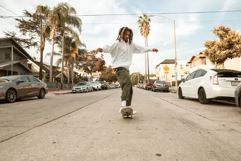 African American man skateboarding down a sunny urban street lined with palm trees.