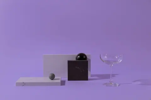 Abstract minimalist composition of geometric shapes and a glass, set on a pastel background.