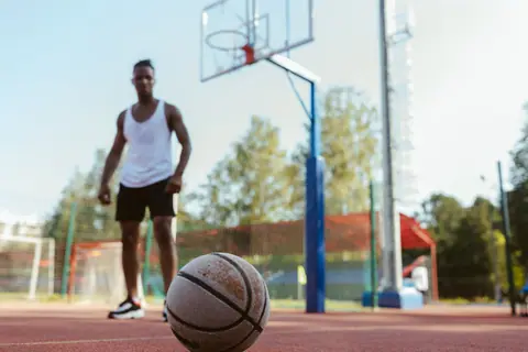 Basketball player on outdoor court preparing to play during daylight.