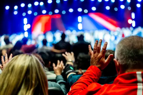A lively audience raising hands at a colorful live concert with bright stage lights.