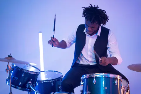 A musician passionately playing a drum set under vibrant studio lighting.