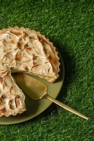 Sliced lemon meringue pie with golden crust on grass, served with gold cake server.