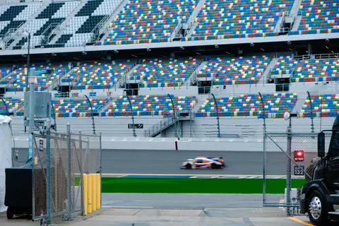 Blurred race car speeding past colorful bleachers at a famous track.