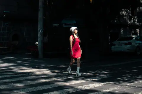 Stylish woman in red dress crossing a city street during the day, showcasing urban fashion.