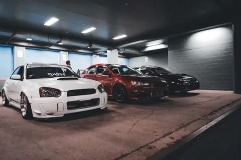 A trio of modified sports cars parked inside a dimly lit underground garage.