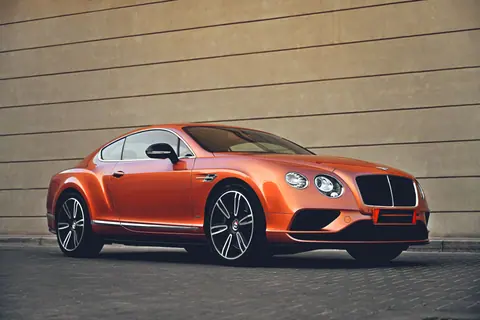 Elegant orange Bentley car parked in front of a modern architectural wall, showcasing luxury and style.