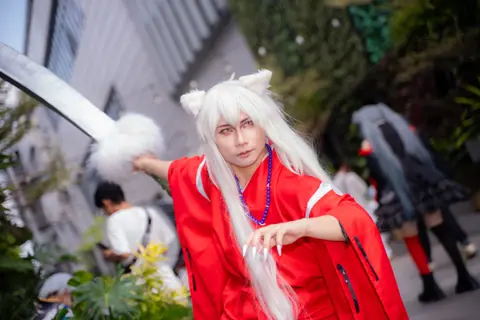 Dynamic cosplay of character in red kimono wielding a sword at an outdoor event.