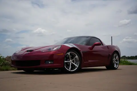 A sleek red Corvette sports car parked on a road with a picturesque sky backdrop.
